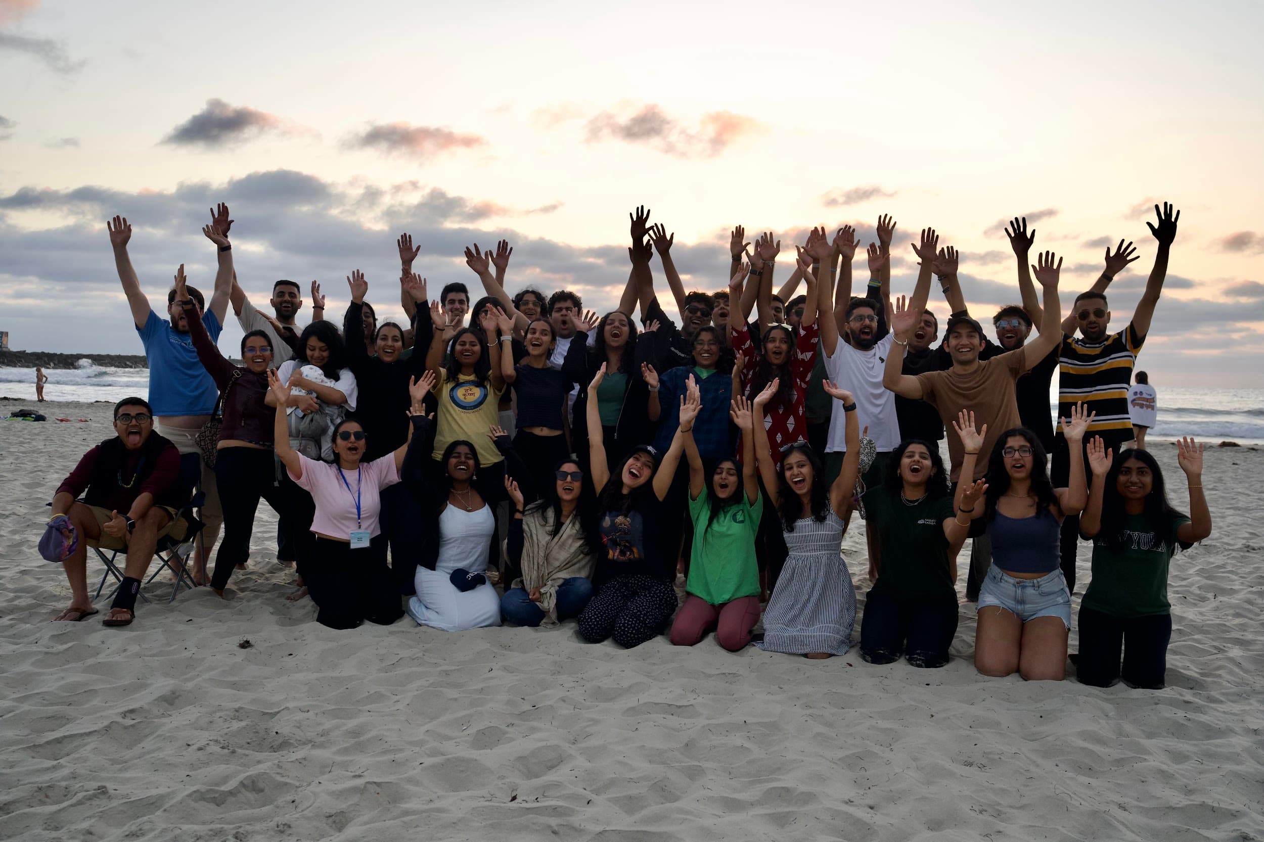A full retreat group standing on the beach at sunset with their arms raised