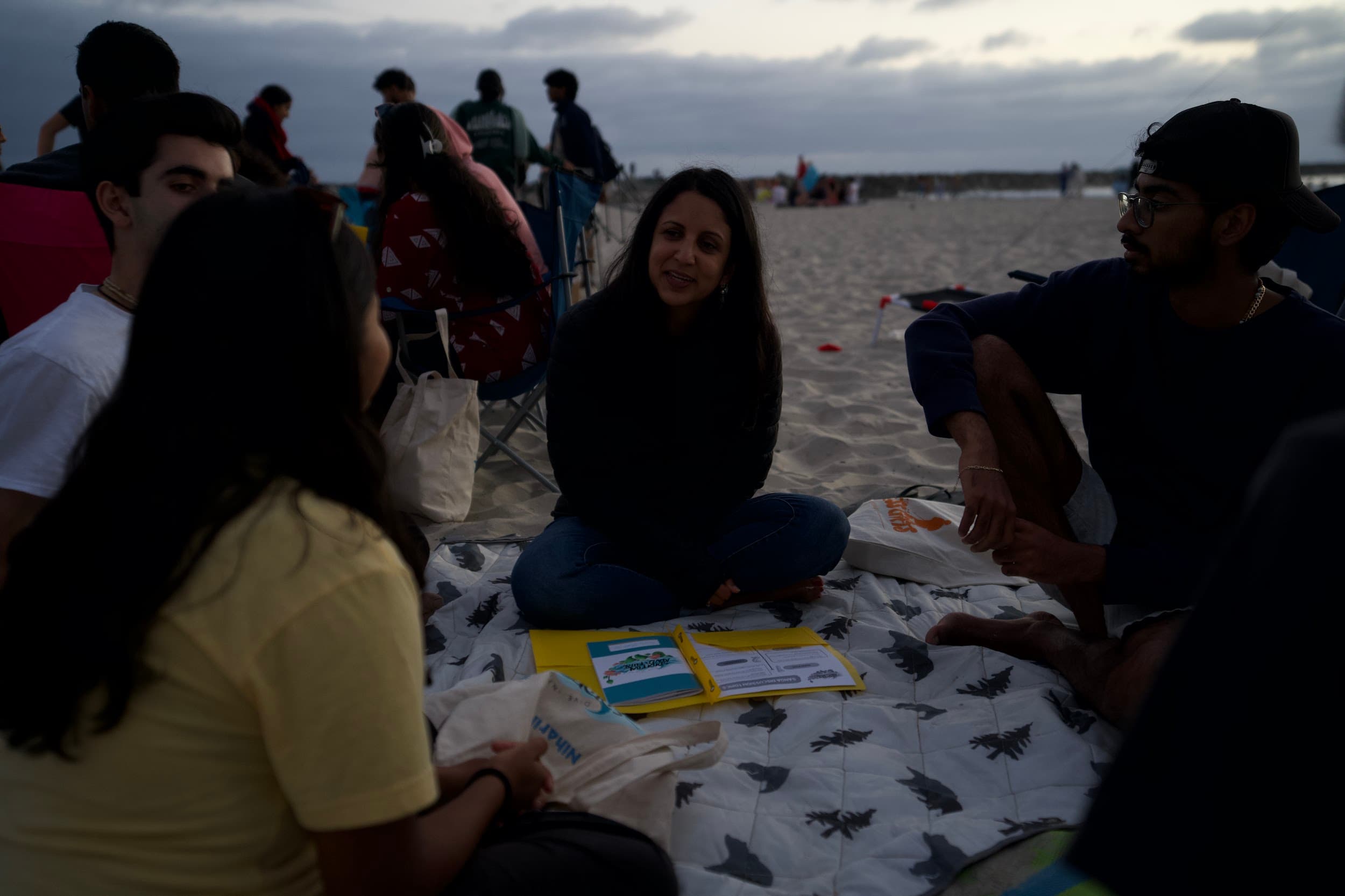 A small group talking on a blanket on the beach at dusk